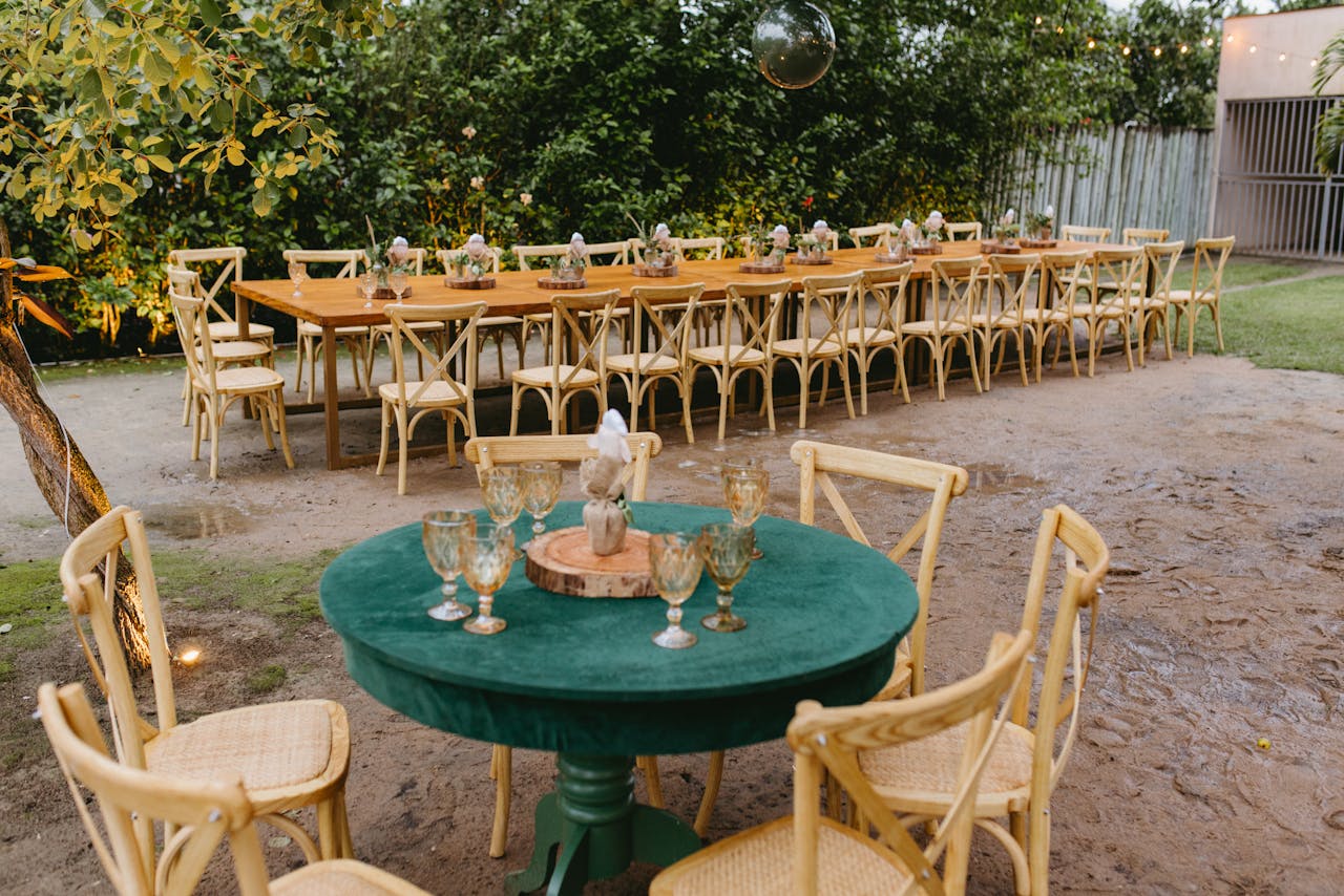 Elegant outdoor dining arrangement with wooden tables and chairs on a rustic garden setting.